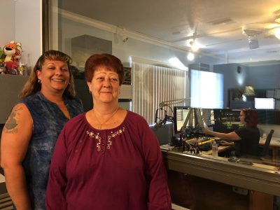 Linda Corso is the station owner of KRDE, her niece Mindy Ensey is the station manager both pose for a photo while Lindsay Chesney records the weather forecast for the upcoming week in the sound booth.
