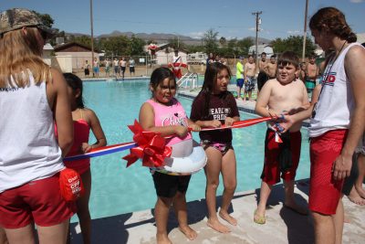 Kids hold the ribbon while the Kearny Pool managers cut the ribbon during the grand reopeninig.