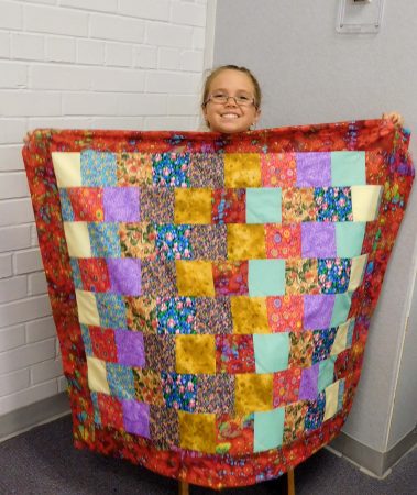 Young seamstress Nevaeh shows off her quilt made at Teen Sew Cool.